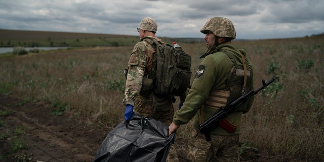 Ukrainian national guard servicemen carry a bag containing the body of a Ukrainian soldier in an area near the border with Russia, in Kharkiv region, Ukraine, Monday, Sept. 19, 2022. In this operation seven bodies of Ukrainian soldiers were recovered from what was the battlefield in recent months. 