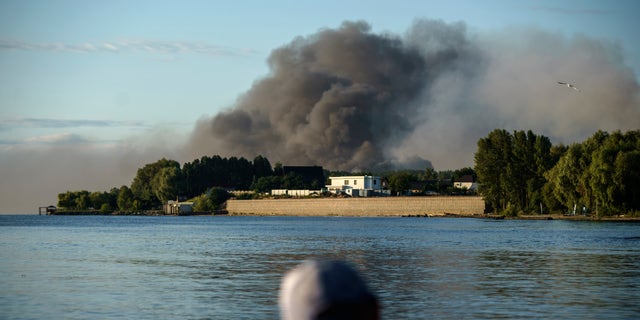 A fisherman watches smoke rise after Russian forces launched a missile attack on a military unit in the Vyshhorod district on the outskirts of Kyiv, Ukraine, Thursday, July 28, 2022. 