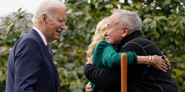 President Biden looks on as first lady Jill Biden hugs Dale Haney, the chief White House groundskeeper (right), during a tree-planting ceremony on the South Lawn of the White House.