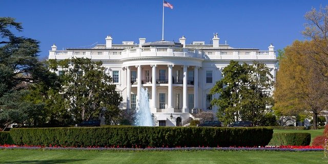The White House lawns are beautifully landscaped lawns with flowers, fountains and blooming trees in foreground.