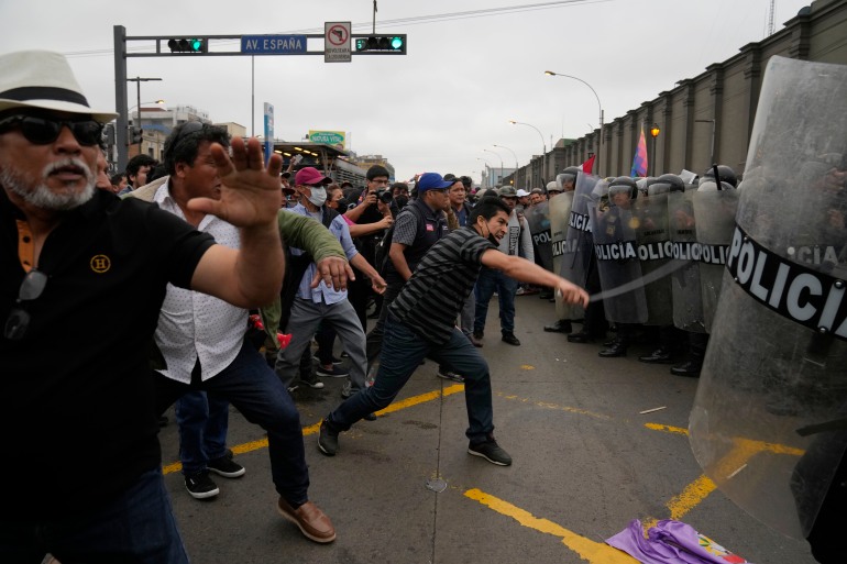 Supporters of former President Pedro Castillo confront riot police surrounding the police station where Castillo arrived earlier, in Lima, Peru, Wednesday, Dec. 7, 2022. Peru's Congress removed Castillo from office Wednesday, voting to replace him with the vice president, shortly after Castillo decreed the dissolution of the legislature ahead of a scheduled vote to oust him. (AP Photo/Martin Mejia)