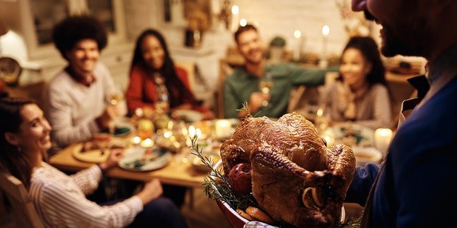 A host is shown serving Thanksgiving turkey to his friends during a meal at the dining table.