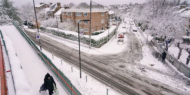 A woman pulls a shopping trolley, in a snow covered residential area in Leytonstone, in London, Monday, Dec. 12, 2022. Snow and ice have swept across parts of the UK, with cold wintry conditions set to continue for days.