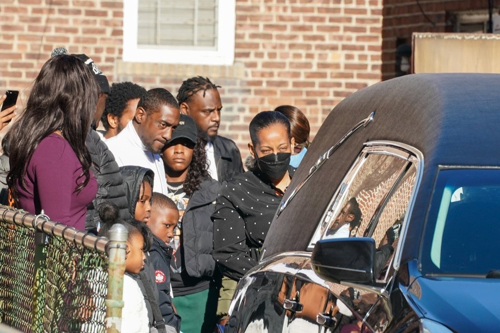 Mourners gathered behind a hearse.