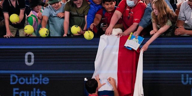 Daniil Medvedev autographs a Russian flag after defeating Marcos Giron at the Australian Open in Melbourne, Monday, Jan. 16, 2023.