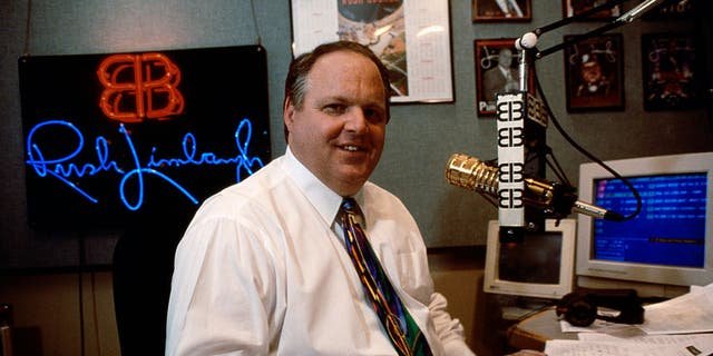 Rush Limbaugh speaking into his famous gold microphone in his studio during his radio show.