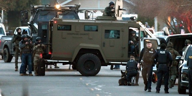 Law enforcement officers aim their weapons at a home during a standoff in Grants Pass, Ore., on Tuesday, Jan. 31, 2023.